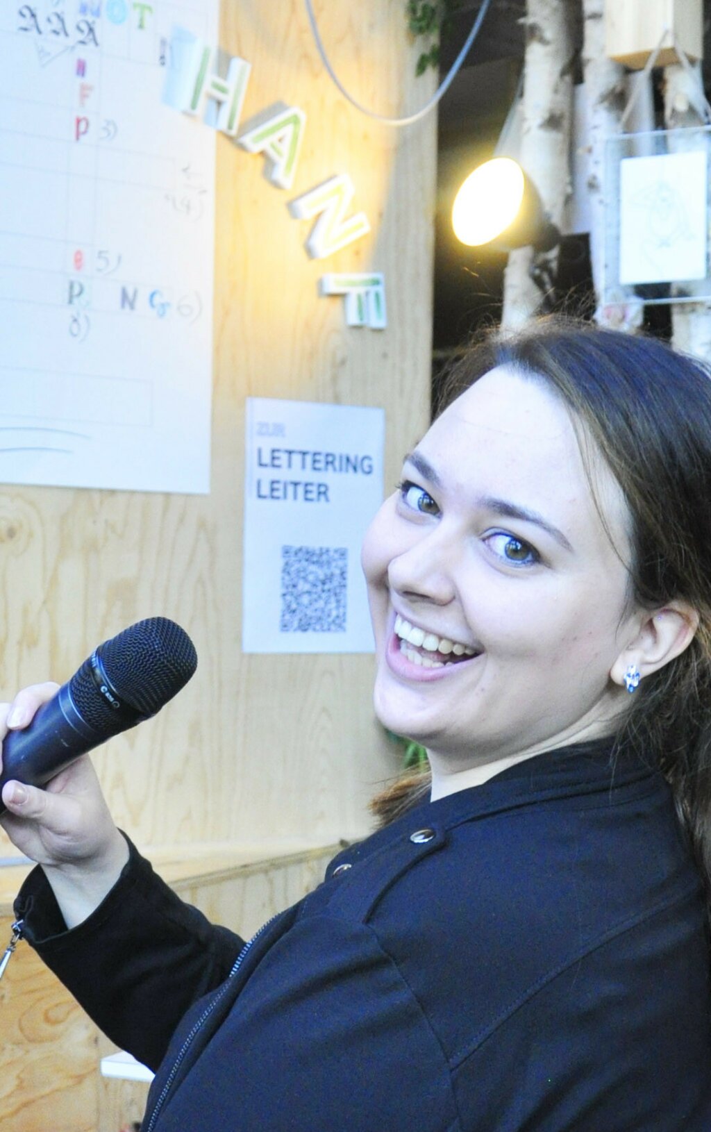 Sharon hält ein Mikrofon in der Hand und lächelt in die Kamera.